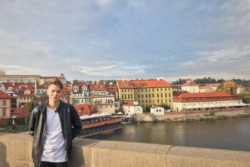 Student stoi z lewej strony. W tle widok na miasto.