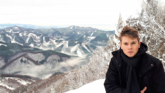 Student stoi z prawej strony. W tle widok na ośnieżone góry.