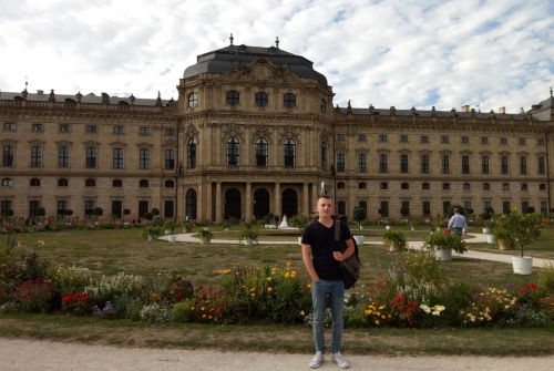 Student stoi. z plecakiem. W tle budynek.