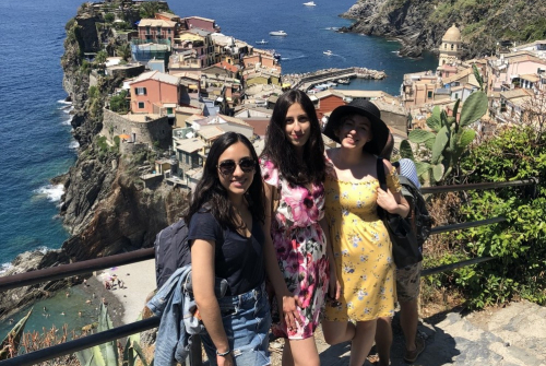 Trzy dziewczyny pozują do zdjęcia . W tle widać morze oraz domy.