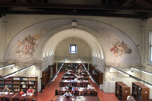 Wnętrze biblioteki widziane z góry. Przy stolikach siedzą ludzie.