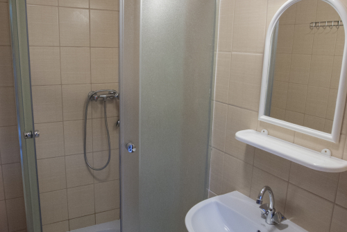 Wnętrze łazienki w akademiku. Po lewej prysznic. Po prawej umywalka, a nad nią lustro.