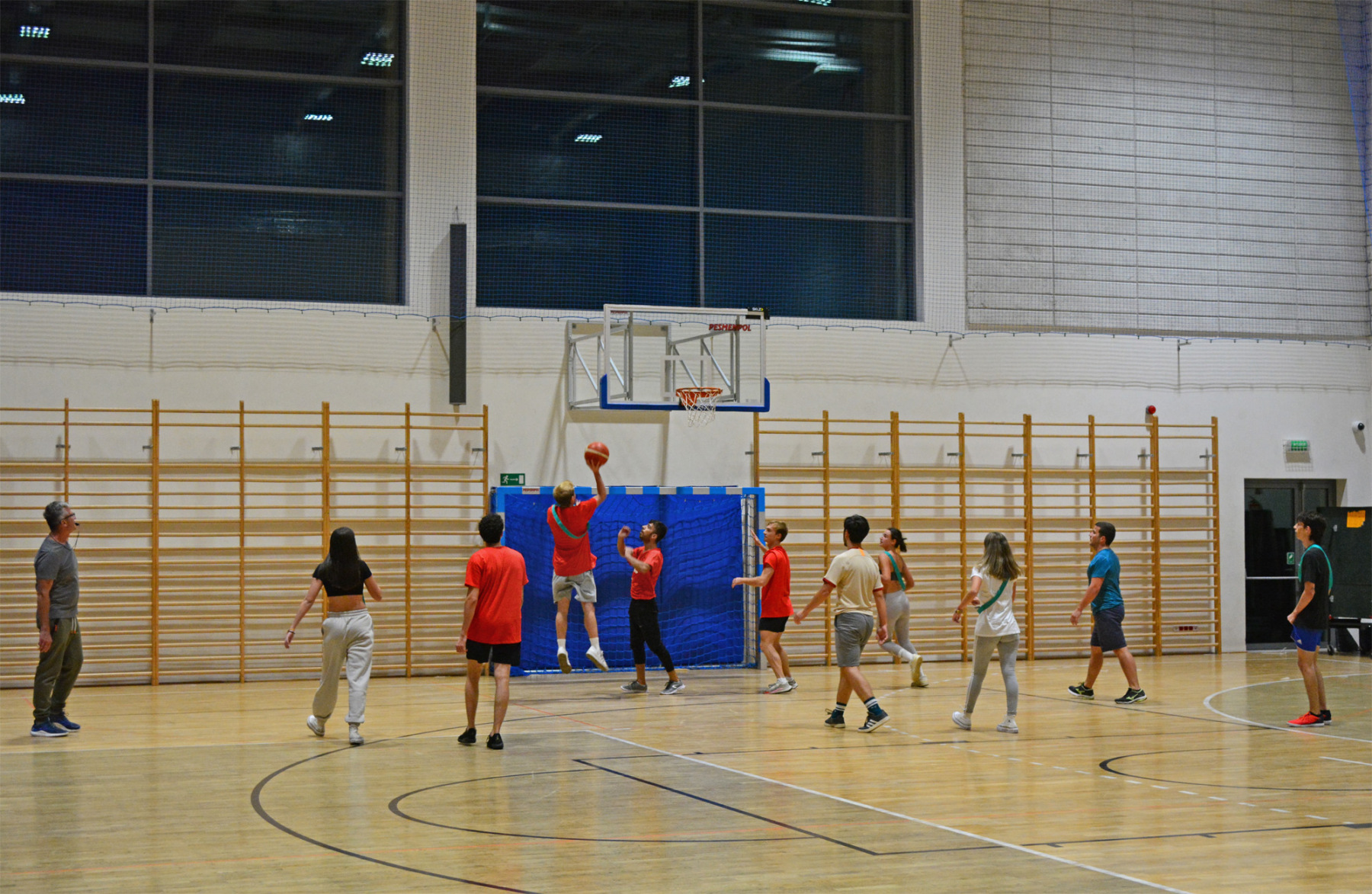 Grupa studentów gra w koszykówkę na hali sportowej.