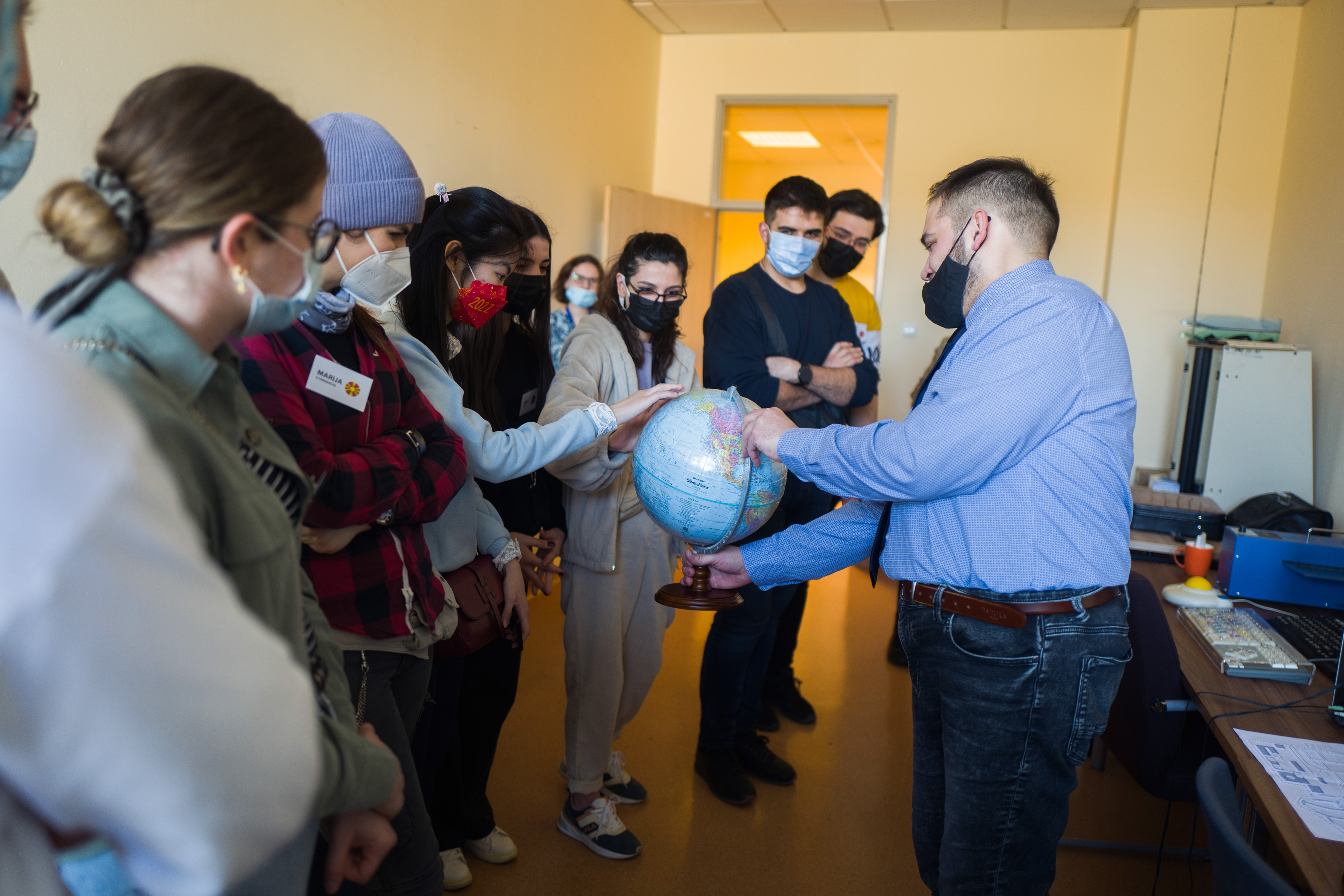 Przewodnik trzyma globus dla osób niewidomych. Otaczają go studenci. Kilka z nich dotyka globusu.