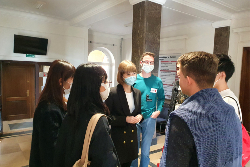 Grupa studentów i koordynator rozmawiają. Stoją zwróceni twarzami do siebie nawzajem.