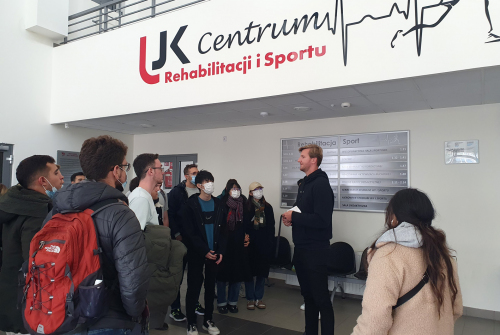 Centrum Rehabilitacji i Sportu. Wykładowca przemawia. Wokół niego stoją i słuchają go studenci.