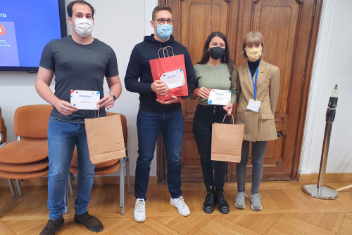 Troje studentów stoi. Trzymają torby z upominkami. Obok nich stoi koordynator.