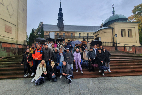 Zdjęcie grupowe.  Część studentów stoi na schodach, pozostali kucają. W tle rzeźba Katedra w Kielcach.