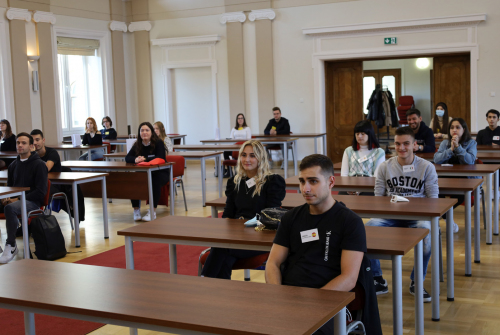 Studenci siedzą. Ławki ustawione są w rzędach. Bliski kadr. Widać dokładnie twarze studentów.