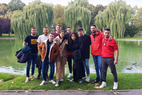 Grupa studentów stoi w parku. W tle drzewa i zbiornik wodny.