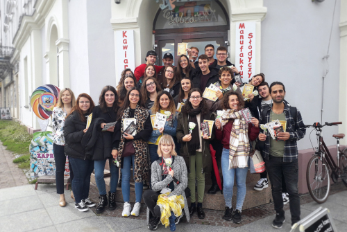 Grupa studentów i koordynatorów stoi przed budynkiem Manufaktury Słodyczy