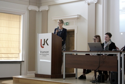 Pani Rektor Monika Szpringer, profesor UJK, w postawie stojące przemawia przy mównicy. Po prawej siedzą pracownicy.