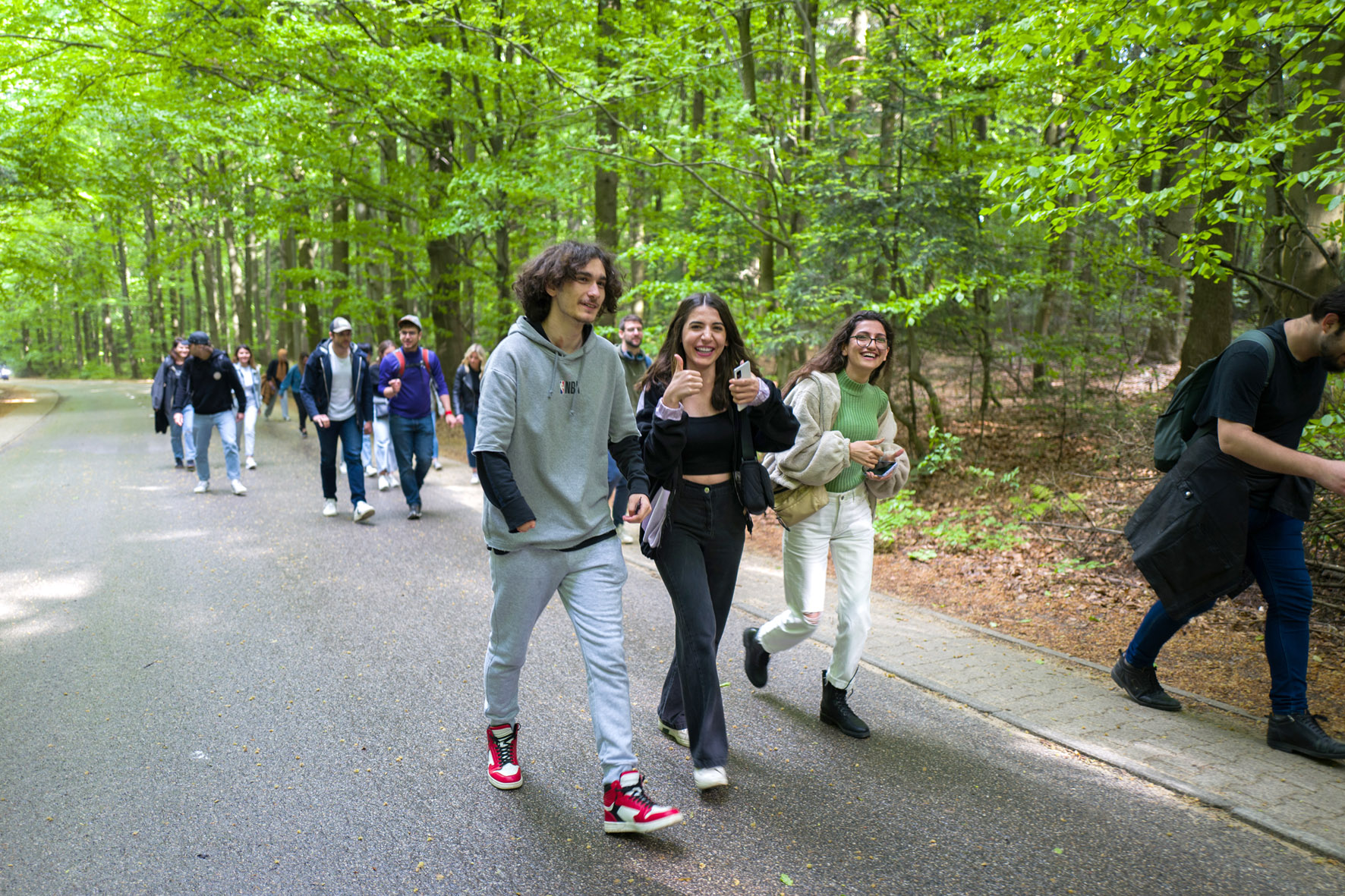 Uśmiechnięci studenci idą przez park. W tle drzewa.